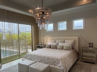A luxurious master bedroom with a crystal chandelier, large glass doors, and a poolside view for ultimate relaxation.