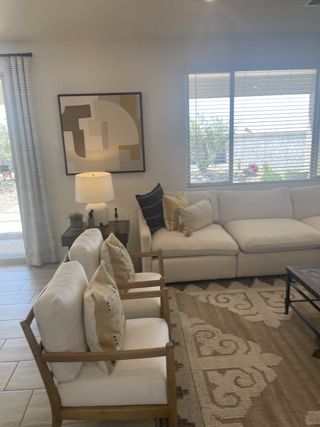 A cozy living room with a white sectional, abstract art, patterned rug, and natural light from large windows.