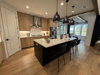 A modern kitchen with sleek wood cabinets, an island, pendant lighting, and scenic views from large windows.