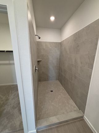 Model Home A modern shower with gray tiling and sleek fixtures opening into a carpeted closet area.