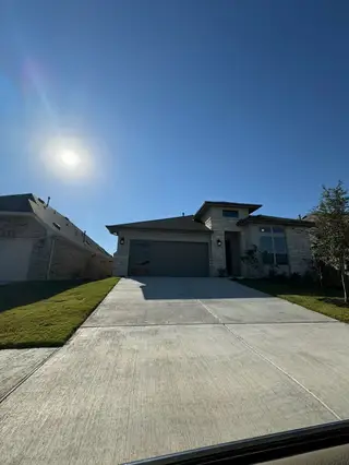 A modern stone-accented home with a spacious driveway in Sunfield by Brightland Homes (Buda, TX).