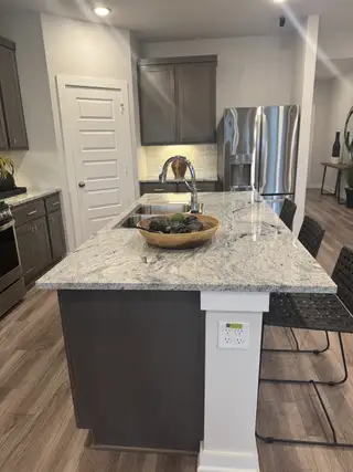 A modern kitchen featuring a granite countertop island, sleek cabinetry, and stainless steel appliances.