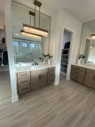 Model Home A modern bathroom with sleek wood cabinetry, elegant mirrors, and stylish lighting fixtures.