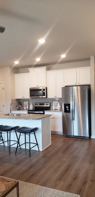 A modern kitchen with white cabinets, stainless steel appliances, granite countertops, and stylish bar stools.