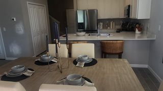 A modern dining area with a wooden table, elegant tableware, and a view of a sleek kitchen with stainless steel appliances.