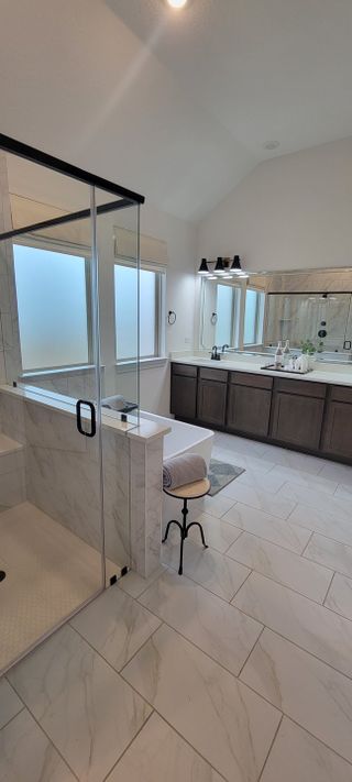 Elegant bathroom with marble tiles, a spacious glass shower, sleek double vanity, and modern lighting fixtures.