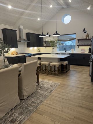 Model Home A modern kitchen with vaulted ceilings, dark cabinets, a central island, and stylish pendant lighting over a cozy dining area.