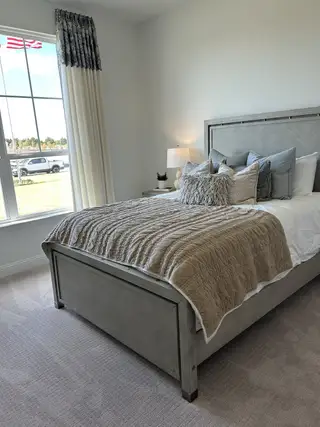 A cozy bedroom with a stylish gray bed, plush pillows, elegant curtains, and a soft carpet for a serene atmosphere.