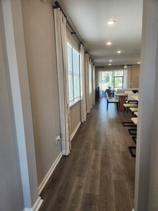 A bright hallway with elegant drapes, warm wood flooring, and modern recessed lighting leading to a cozy dining area.