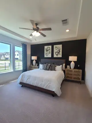 A cozy bedroom with a dark accent wall, elegant ceiling fan, and plush carpeting for a comfortable retreat.