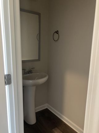 A compact bathroom features a pedestal sink, framed mirror, and sleek towel ring on dark wood flooring.