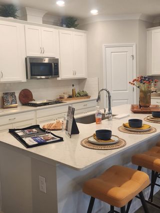 Model Home A modern kitchen featuring white cabinetry, a sleek island with seating, and stainless steel appliances.