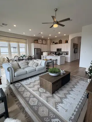 An open living area with a cozy sofa, patterned rug, and modern kitchen featuring white cabinetry and stainless appliances.
