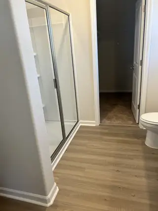 Model Home A modern bathroom featuring sleek wood flooring, a glass-enclosed shower, and an adjacent walk-in closet.