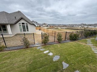 A serene backyard with lush greenery, iron fencing, and scenic views in Veramendi by Perry Homes (New Braunfels, TX).
