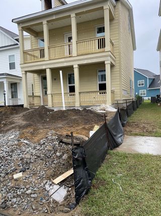 Street view A charming yellow home under construction with dual porches in Oak Bluff by Dream Finders Homes (Charleston, SC).