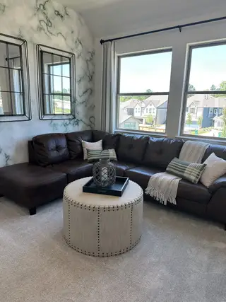 Model Home A cozy living room with a leather sectional, marble accent wall, and large windows overlooking suburban homes.