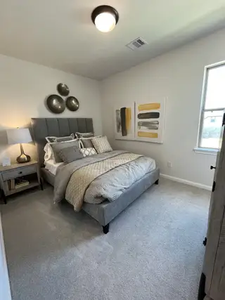 Model Home A cozy bedroom featuring a gray upholstered bed, modern wall art, and soft lighting.