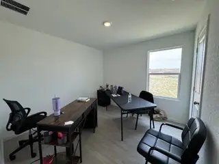 Model Home A bright office space with a wooden desk, black chairs, and a window overlooking a grassy landscape.