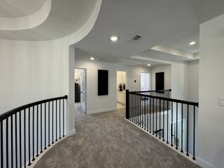 A modern upstairs hallway with sleek black railings, plush carpet, and recessed lighting, offering a bright, airy ambiance.