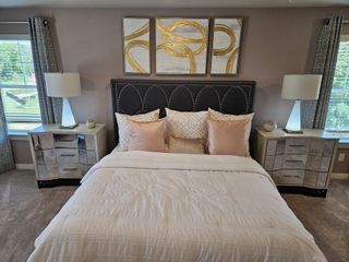 Model Home A cozy bedroom with elegant wall art, a chic upholstered headboard, mirrored nightstands, and soft lighting.