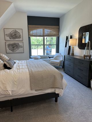 A cozy bedroom with a stylish bed, modern dresser, and ample natural light from a large window with woven blinds.