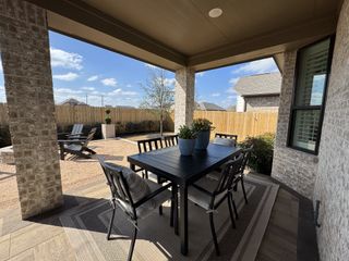 A cozy covered patio with a black dining set overlooks a fenced backyard, ideal for outdoor relaxation and entertainment.