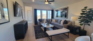 Model Home A stylish living room with a cozy gray sectional, black accents, artful decor, and large windows letting in natural light.