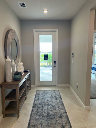 A bright entryway with a modern console table, decorative accents, and a large mirror, leading to a sunlit outdoor view.