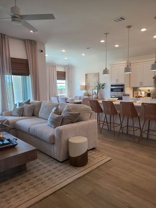 An elegant open living space features a cozy sofa, airy drapes, and a modern kitchen with stylish bar seating and pendant lights.