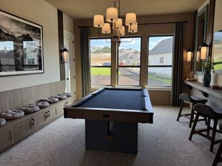 A stylish game room featuring a sleek black pool table, plush seating, and elegant lighting with scenic backyard views.