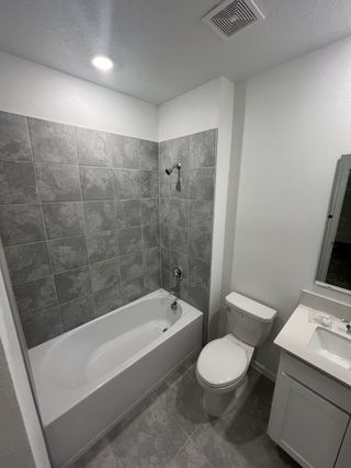 A modern bathroom featuring a sleek bathtub, gray tiled walls, and a compact vanity.