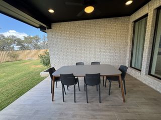 A cozy covered patio with a dining set, white brick walls, and a view of a fenced backyard.