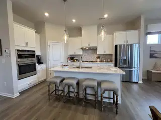 Model Home A modern kitchen with sleek white cabinetry, stainless steel appliances, and a spacious island with pendant lighting.