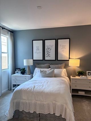 A cozy bedroom with a plush bed, soft gray walls, elegant artwork, and soft lighting from twin bedside lamps.