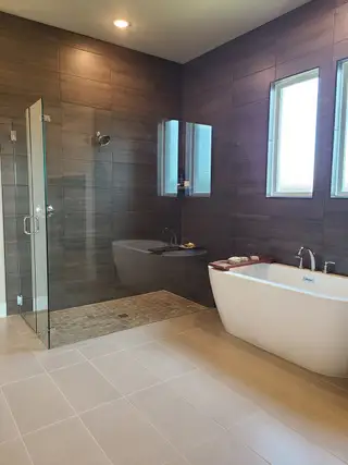 Model Home A modern bathroom with a glass-enclosed shower, dark wood tiles, and a sleek freestanding bathtub.