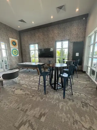A chic game room featuring a patterned carpet, high-top table with metal chairs, and a flat-screen TV for entertainment.