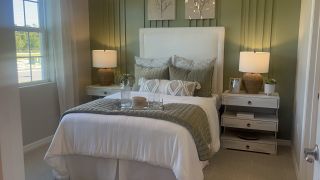 A cozy bedroom with a green accent wall, elegant lamps, and plush bedding, creating a serene atmosphere.