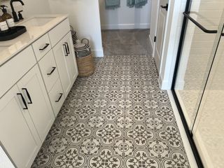A chic bathroom features patterned tile, a sleek white vanity, and modern black fixtures.