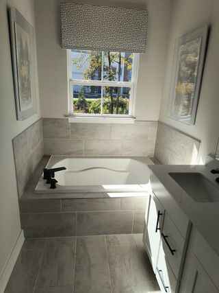 Model Home A cozy bathroom with a built-in tub, elegant tile flooring, and natural light streaming through a decorated window.