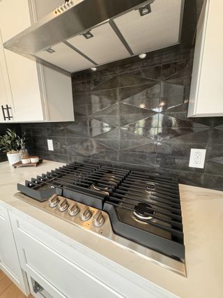 A modern kitchen with a sleek black tile backsplash, stainless steel range hood, and a gas stove with elegant white cabinetry.