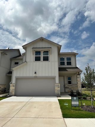 A modern white home with stone accents and a spacious driveway in Wellspring by Clark Wilson Builder (Round Rock, TX).