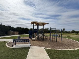 A charming playground with modern equipment in Bryson by Highland Homes, Leander, TX, surrounded by lush greenery and benches.