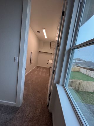 A bright and spacious laundry room with built-in shelving, plush carpeting, and natural light from an adjacent window.