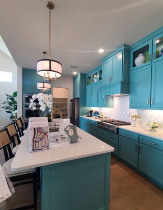 A modern kitchen featuring vibrant teal cabinets, elegant pendant lighting, and a spacious island with seating.