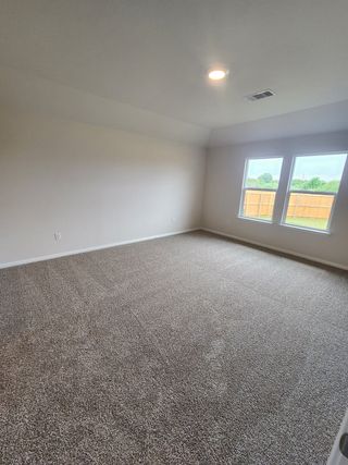 Model Home A spacious carpeted room with neutral tones, featuring a large window offering natural light and a serene backyard view.