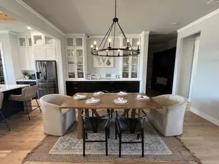 Model Home A chic dining area with a wooden table, plush beige chairs, open shelving, and a modern black chandelier.