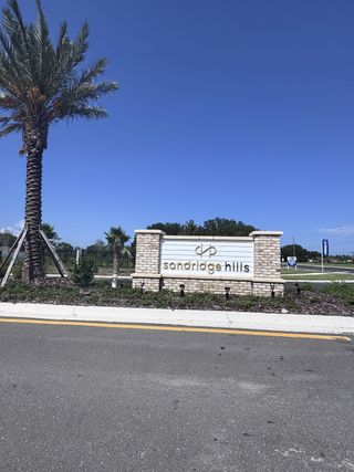 Street view Charming entrance to Sandridge Hills by Mattamy Homes in Green Cove Springs, FL, featuring a stylish stone sign and palm trees.