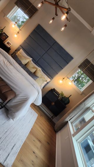 A modern bedroom with a striking blue upholstered headboard, pendant lighting, and warm wood flooring for a cozy and stylish retreat.