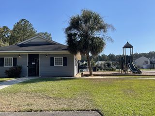 Charming gray clubhouse and playground in Oakley Pointe by Eastwood Homes, Moncks Corner, SC, surrounded by lush greenery.